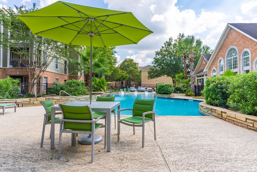 Affordable Houston Texas Apartments – Gramercy Park – Photo of our apartments have a pool and a patio with chairs and an umbrella