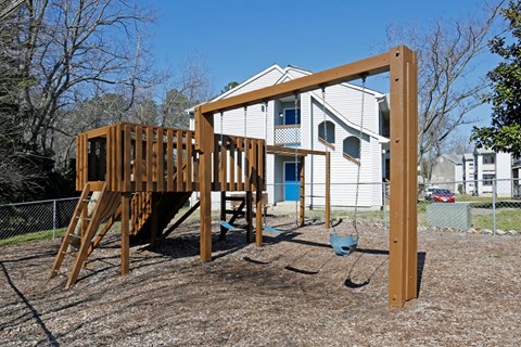 A wooden swing set in front of a white house.