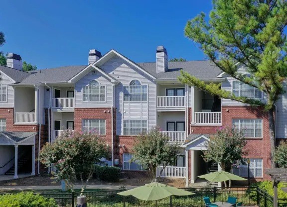 A large apartment complex with a pool and green lawn chairs.