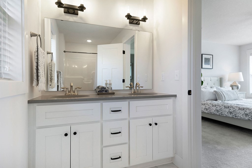A bathroom with a vanity, mirror, and a bed in the background.