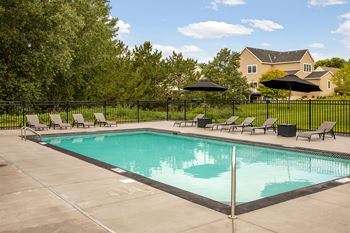A large swimming pool surrounded by a black fence and lounge chairs.