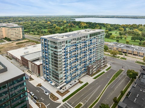 A modern glass building is surrounded by other buildings and a body of water.