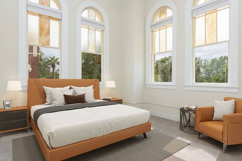Affordable Apartments In San Antonio, TX, With In-Unit Washer And Dryer - The St. John - A Spacious Bedroom With Historic Arched Windows, A Tan Leather Platform Bed, And A Matching Accent Chair.