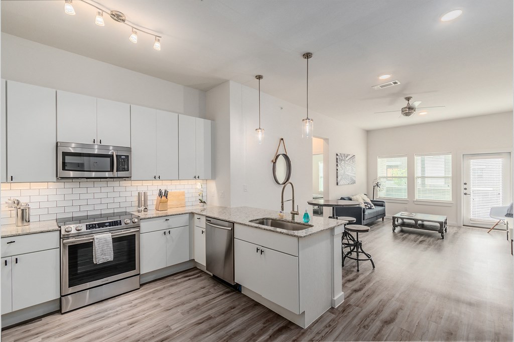 an open kitchen and living room with white cabinets and stainless steel appliances