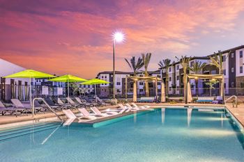 a swimming pool with chaise lounge chairs and umbrellas in front of an apartment building