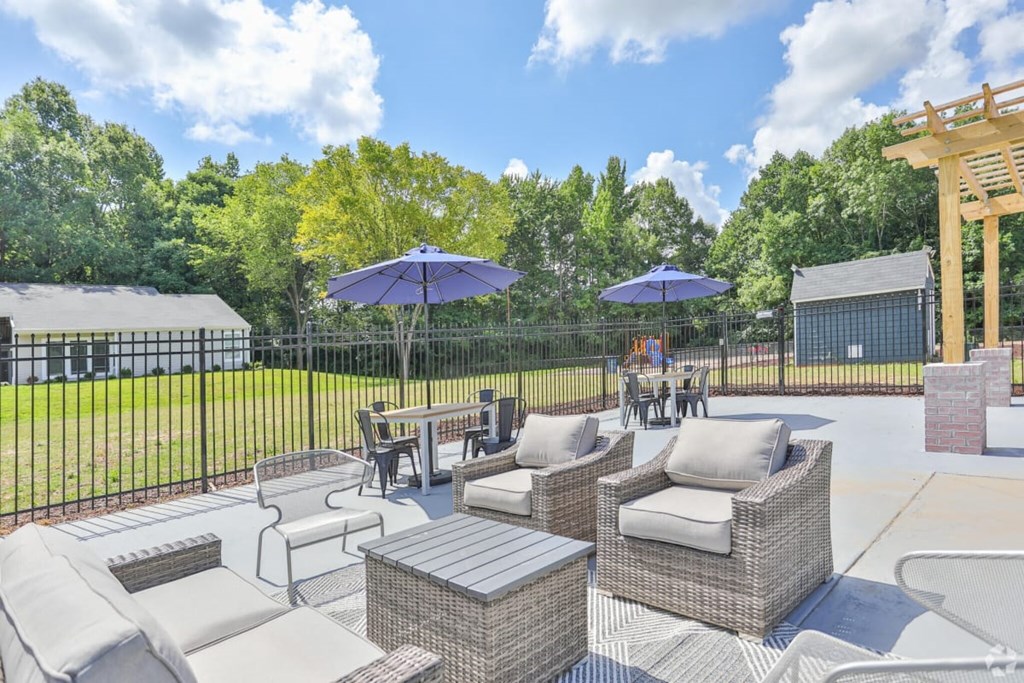 a patio with couches tables and umbrellas in front of a fence