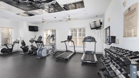 Apartment fitness center with treadmills, ellipticals, stationary bikes, and dumbbell rack.