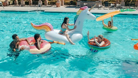 People are enjoying a sunny day at the pool with inflatable unicorn floats.