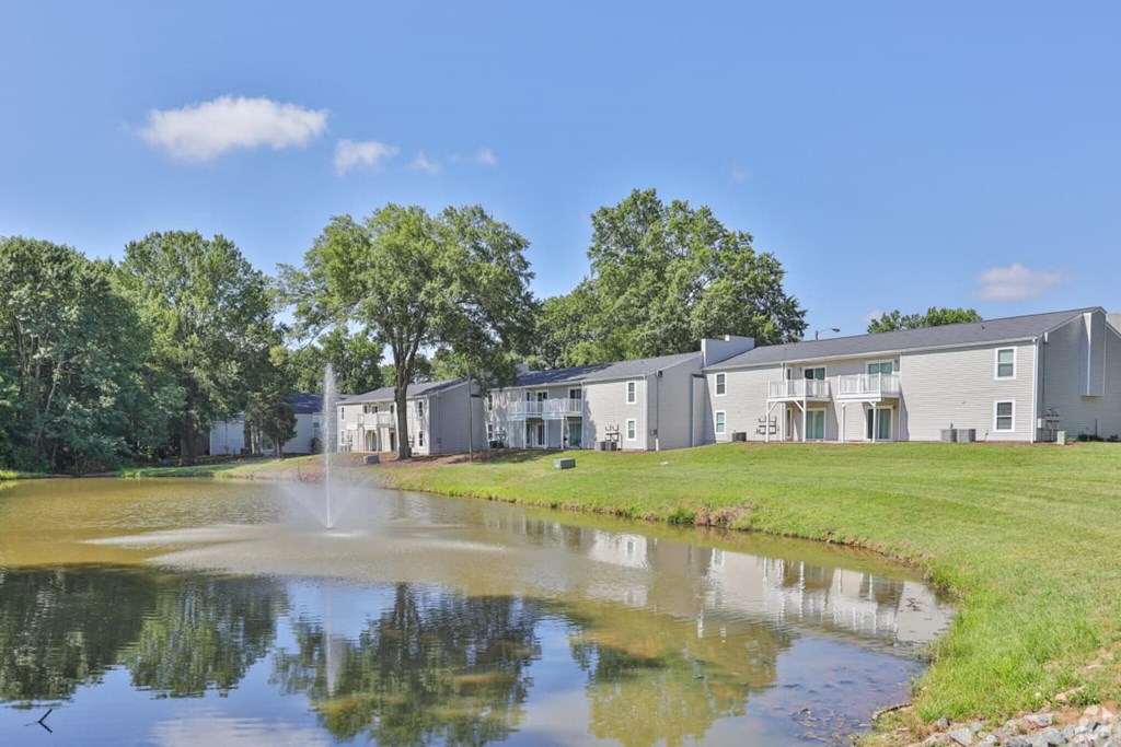 a pond with a fountain in front of a row of condominiums