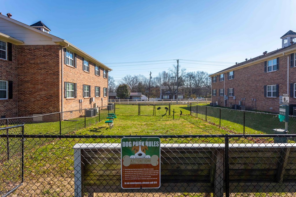 Fenced dog park with agility equipment and posted rules.