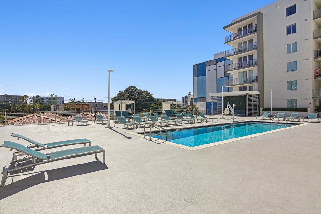 Apartments for Rent in Riverview Miami, FL– Riverview One Apartments -   A large swimming pool with sun loungers and a building in the background.