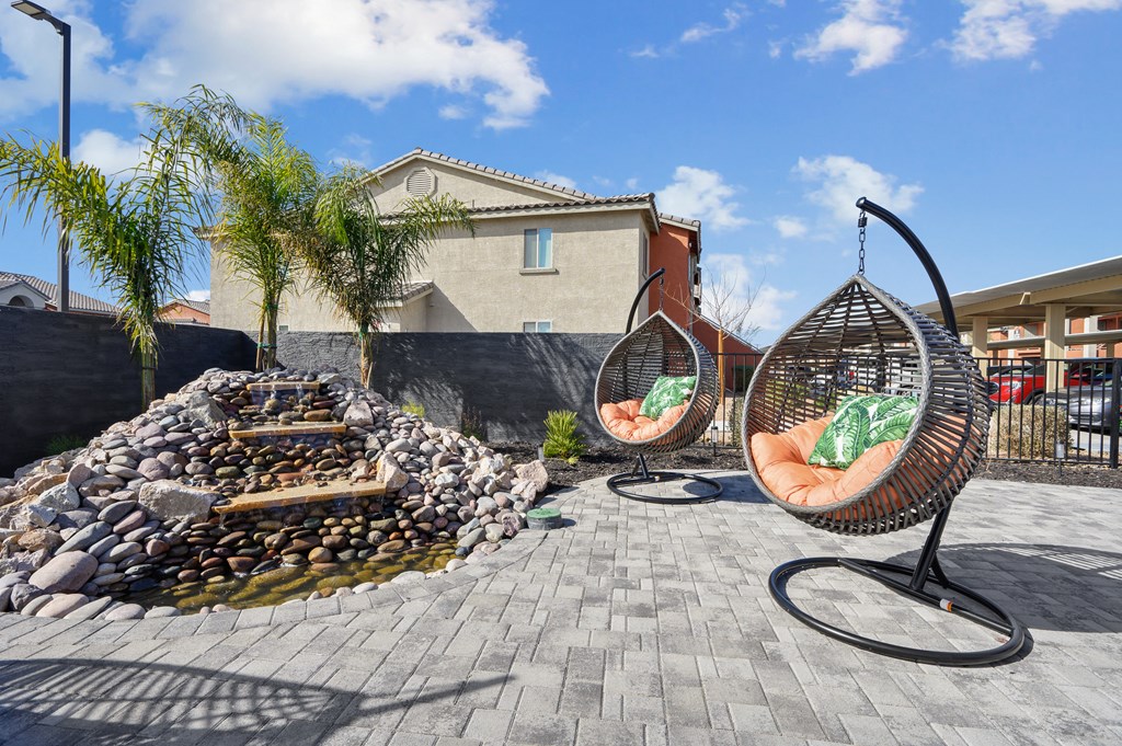 A patio with two hanging chairs and a fire pit.