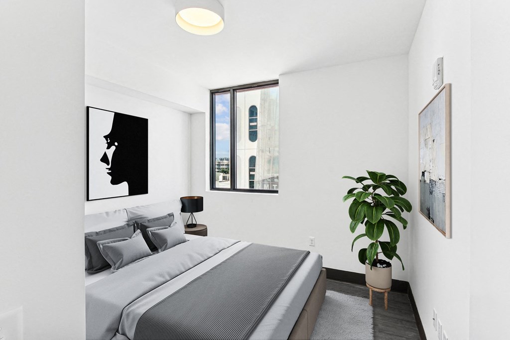 Apartments In Collins Park Miami Florida for Rent – The Anamar at Collins Park - A bedroom with a bed, a potted plant, and pictures on the wall.