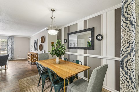 Open-concept dining and living area with a wood dining table, gray accent wall, wood-style flooring, and patterned window curtains