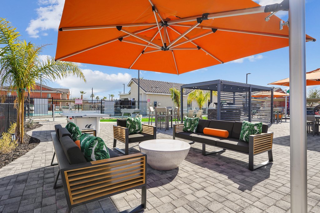A patio with a table, chairs and an orange umbrella.