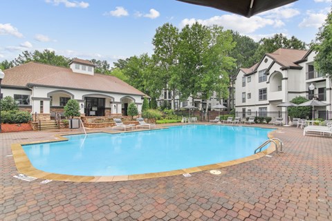 A large outdoor swimming pool surrounded by a brick patio and lounge chairs.