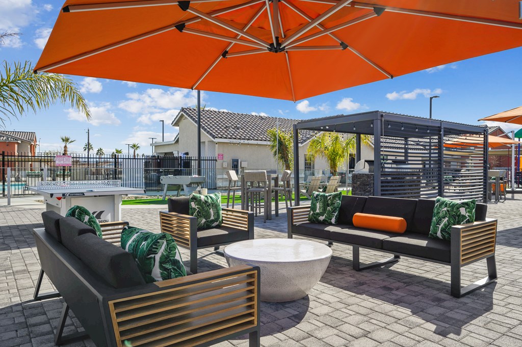 A patio with a table, chairs and a bench under an orange umbrella.