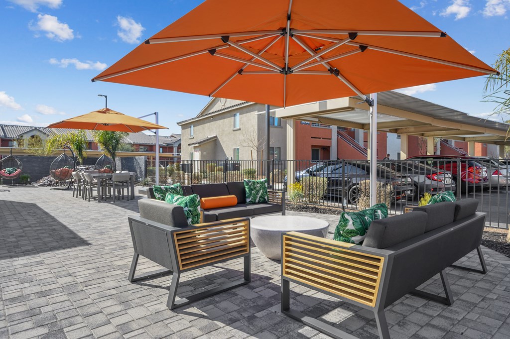 Two chairs and a table are under an orange umbrella.