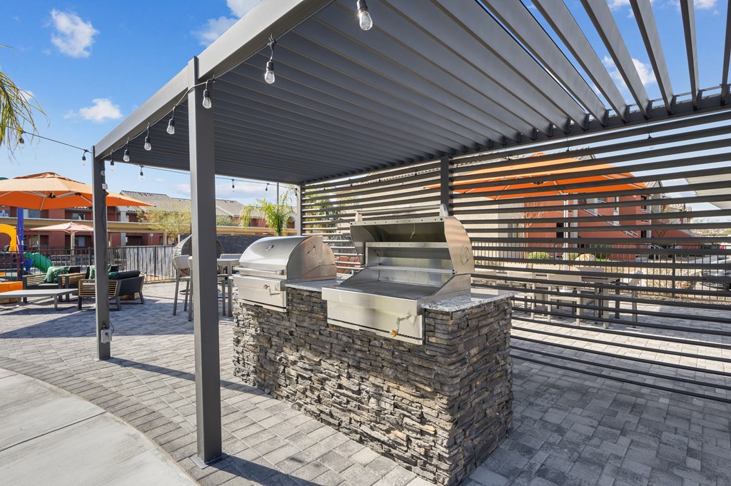 A stone grill is on a patio under a metal roof.