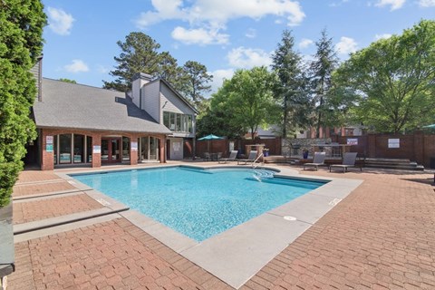 A large swimming pool surrounded by a brick patio and a building in the background.