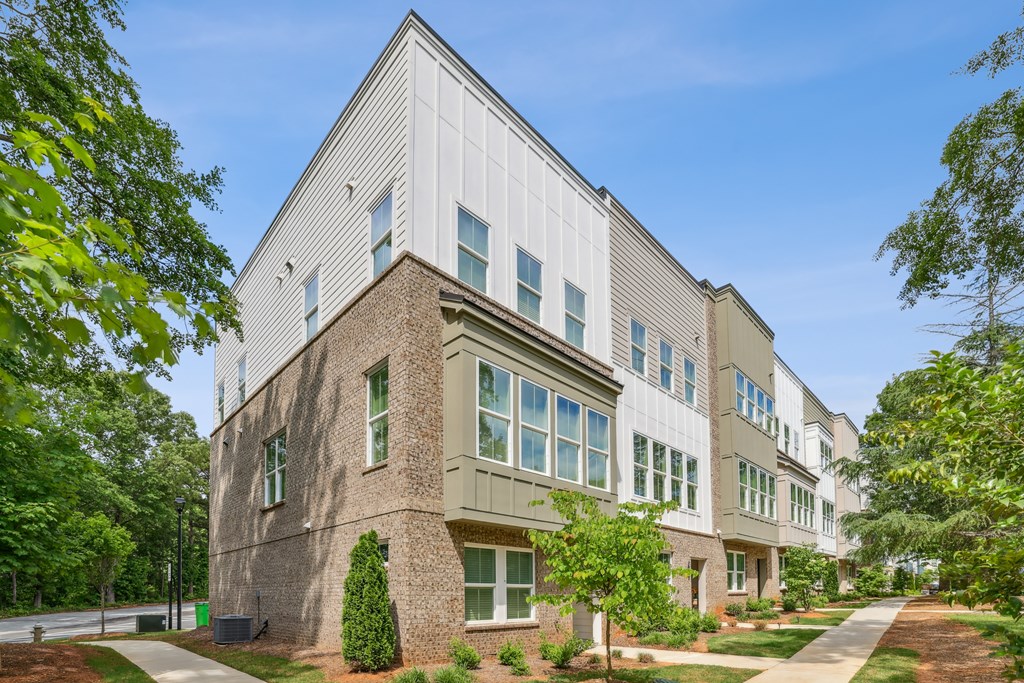A modern building with a mix of white and brown exterior walls, surrounded by greenery and a clear blue sky.