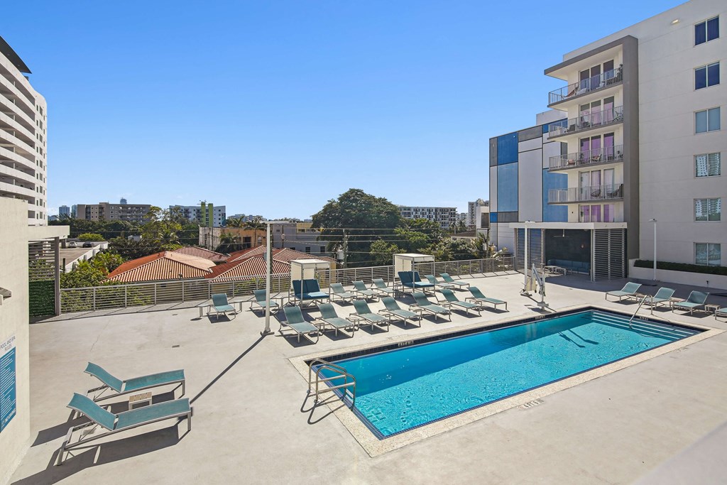 1- & 2-Bedroom Apartments for Rent in Miami, FL – Riverview One Apartments – A swimming pool with sun loungers and apartment buildings in the background.