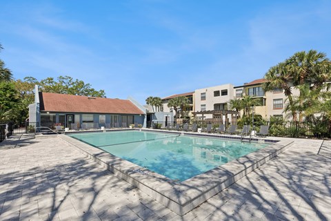 A large swimming pool surrounded by a concrete patio and a building in the background.