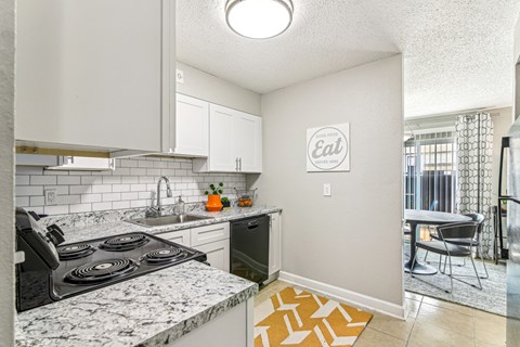 Kitchen with white cabinets, granite-look counters, subway tile backsplash, black electric range, and dining area beyond