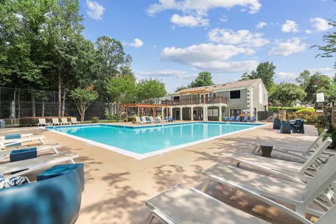 Outdoor swimming pool surrounded by blue lounge chairs, shaded seating, and mature trees at Elliot Norcross