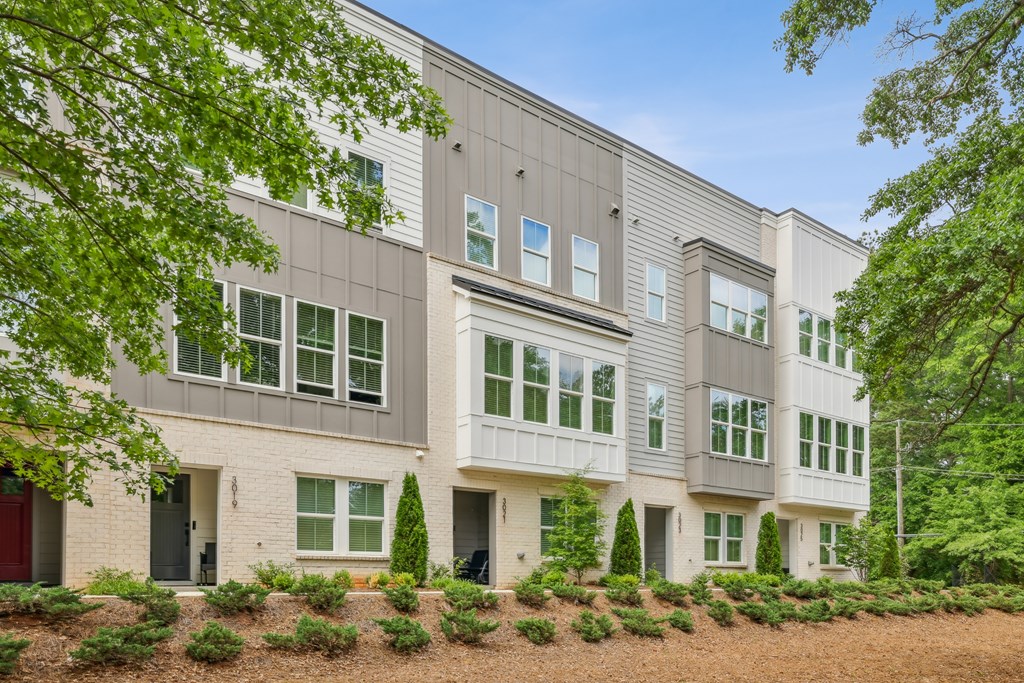 A modern building with a grey facade and white trim is surrounded by greenery.