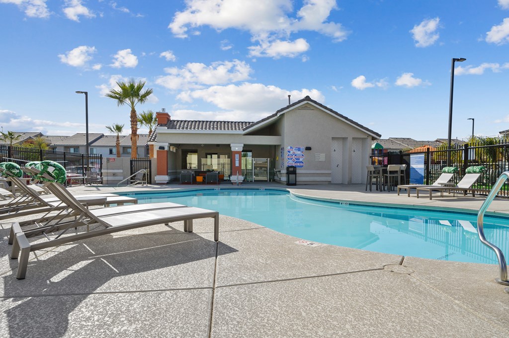 A pool with sun loungers and a building in the background.