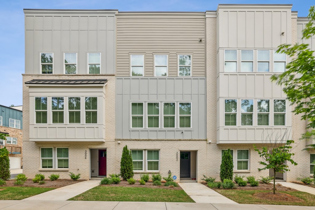 A modern two-story building with a red door and a small tree in front.