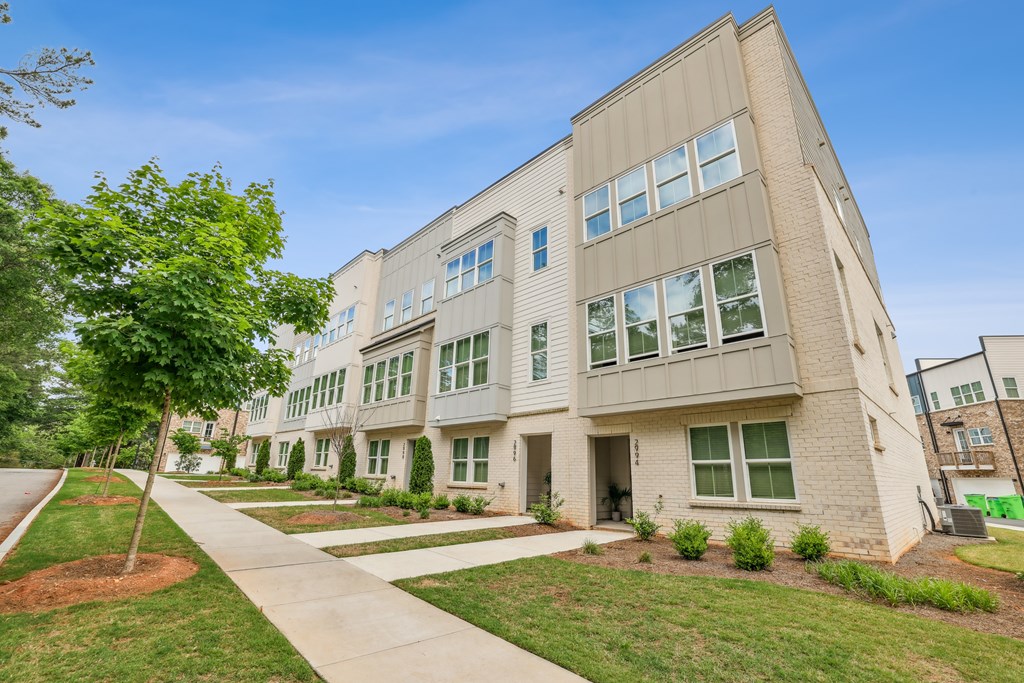 A modern apartment building with a tree-lined sidewalk in front.
