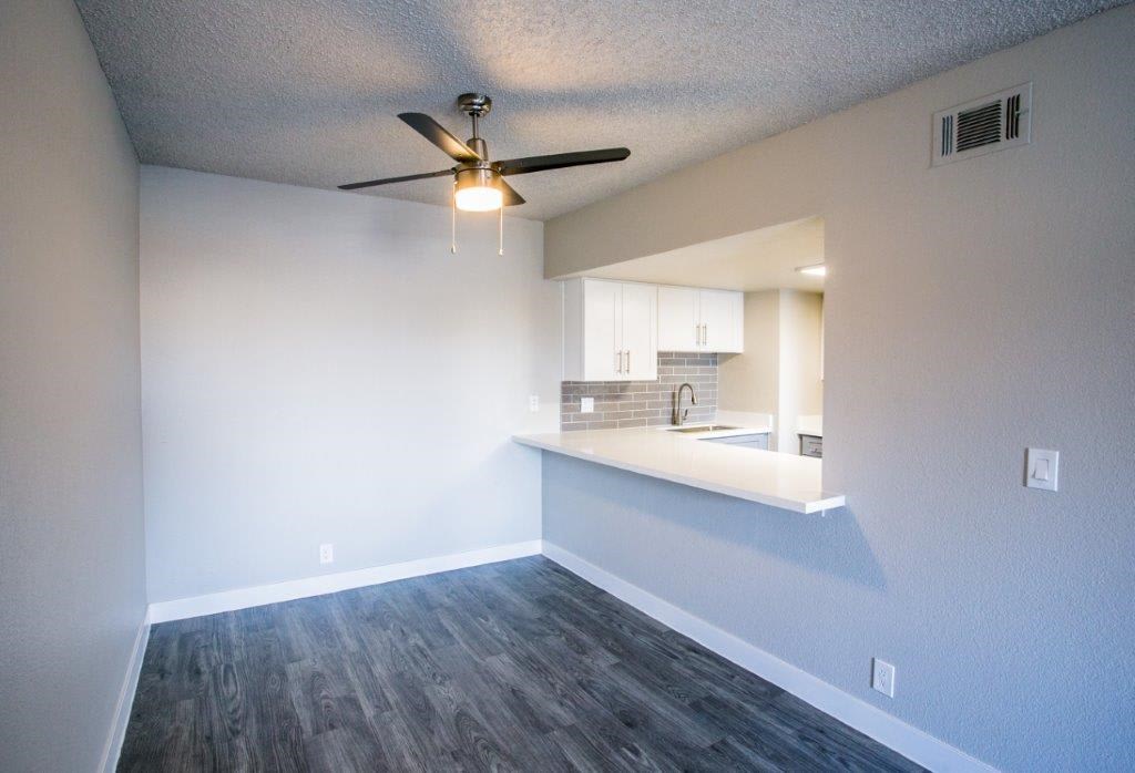 an empty room with a ceiling fan and a kitchen in the background