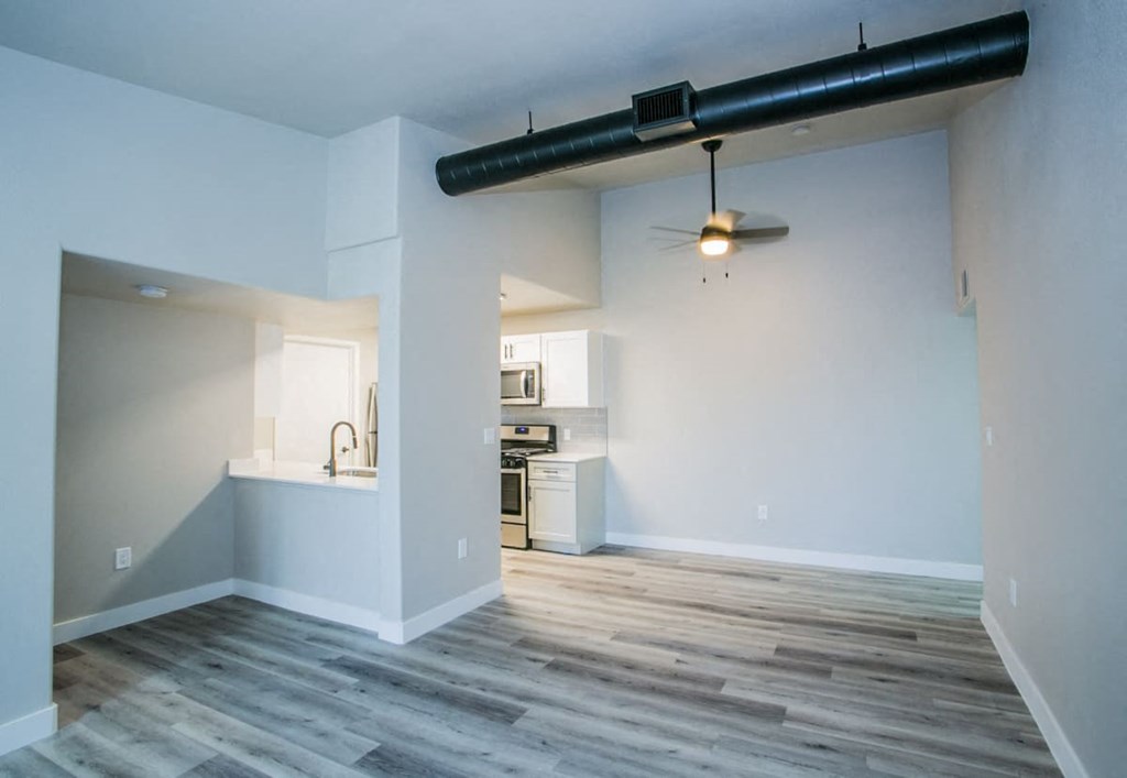 an empty living room with a kitchen in the background