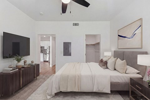 Elegant bedroom showcasing a plush bed with neutral-colored bedding, contemporary decor, and a wall-mounted television, opening into a sleek kitchen area.