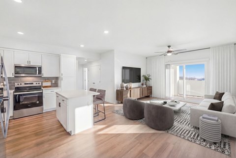 Chic open-plan living area with a modern kitchen, stylish furnishings, and a large wall-mounted TV, exuding comfort and elegance at Summit on Boulder Apartments near Las Vegas