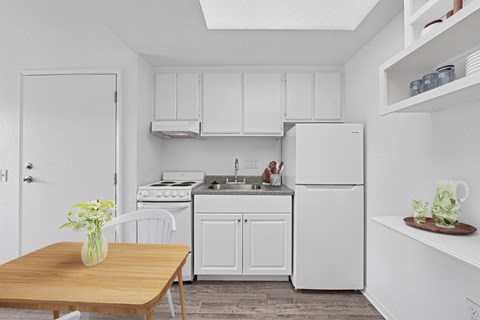 A kitchen with white appliances and a wooden table with a vase of flowers on it.
