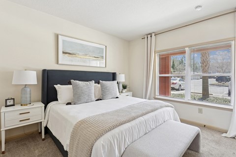 A bedroom with a large bed, a nightstand with a lamp, and a window with a view of the outside.