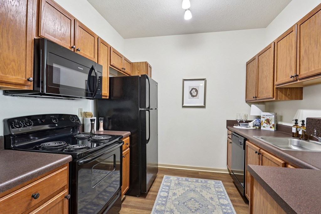 Fully equipped kitchen with black appliances and wood cabinetry in Tattersall Village Apartments, Hinesville, GA