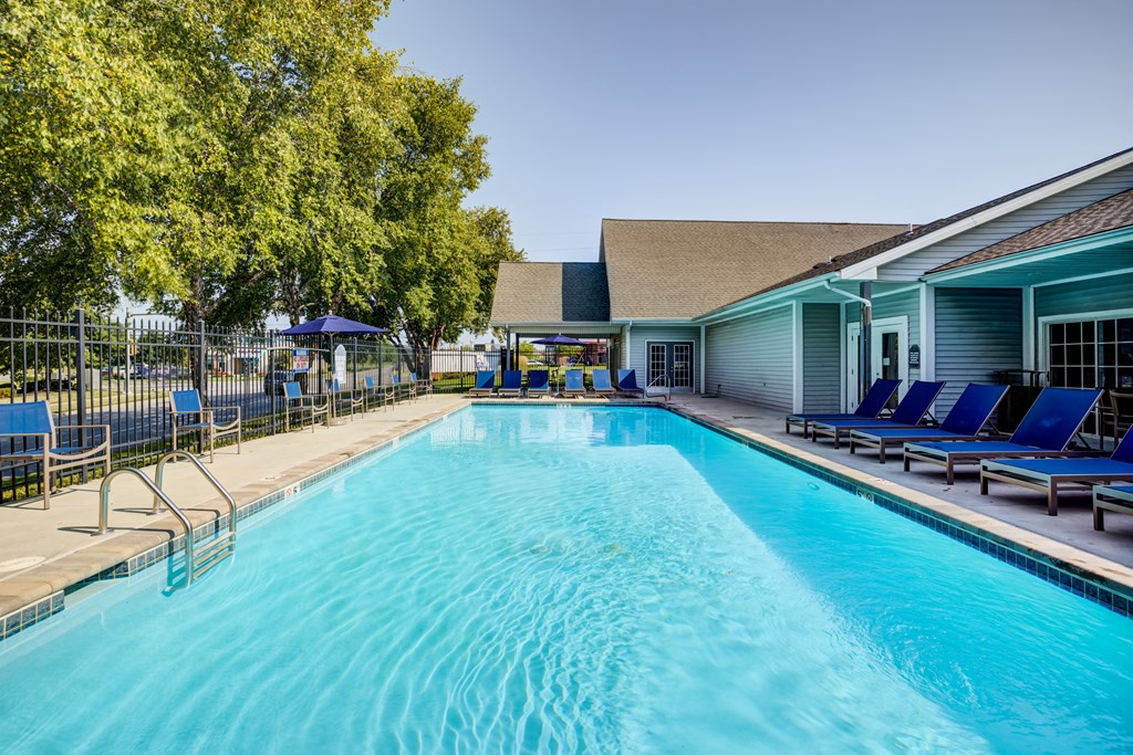 a swimming pool with blue chaise lounge chairs and a building in the background