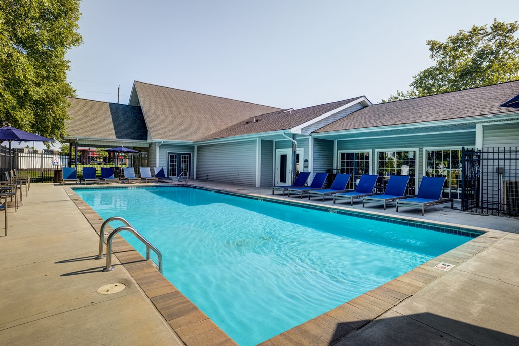 a swimming pool with blue chaise lounge chairs and a building in the background