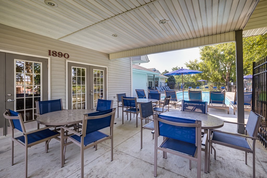 a covered patio with tables and chairs and a pool in the background