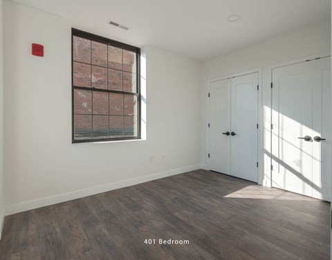 Empty apartment room with hardwood flooring, white walls, and a single large window.