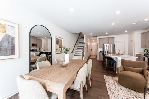 Open-concept townhome living, dining, and kitchen area with modern finishes, wood-style flooring, kitchen island, and staircase at Townes at Olde Birch in Raleigh, NC.