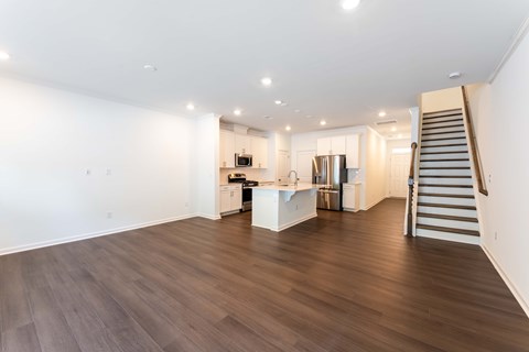 Spacious open-concept townhome living area with wood-style flooring, modern kitchen, stainless-steel appliances, and staircase at Townes at Olde Birch in Raleigh, NC.