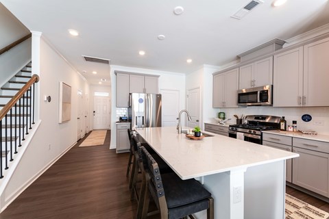 Modern open-concept townhome kitchen with oversized island, stainless-steel appliances, gray cabinetry, and bar seating at Townes at Olde Birch in Raleigh, NC.