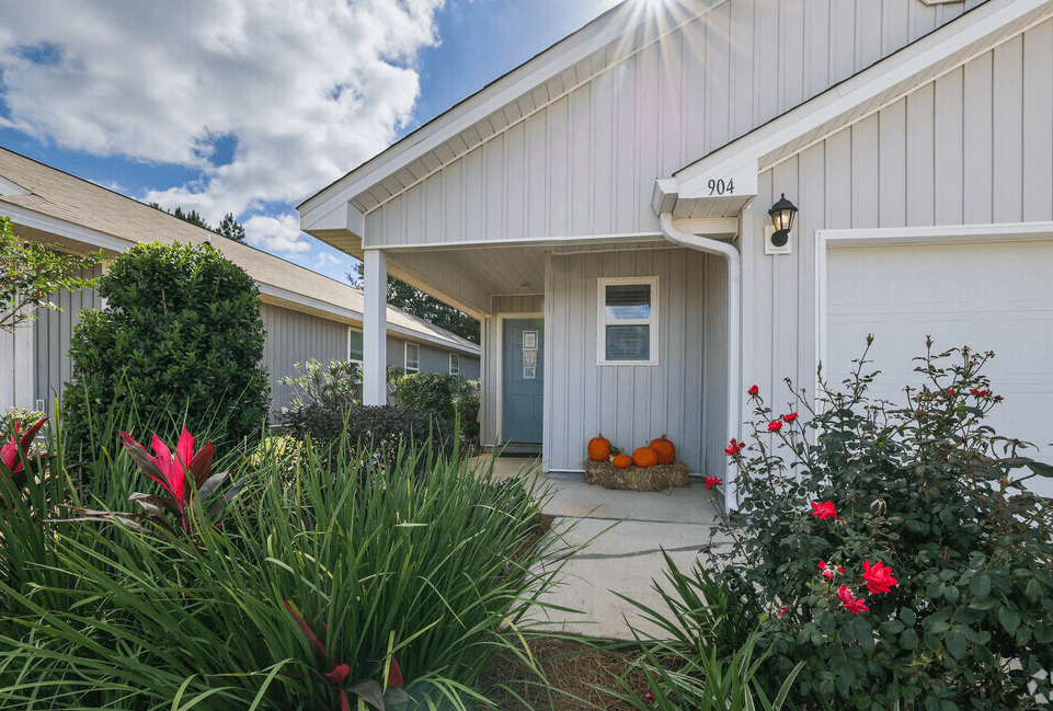 the front of a white house with a patio and flowers