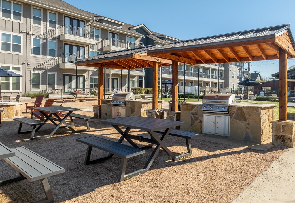 a picnic area with picnic tables and a grill in front of an apartment building