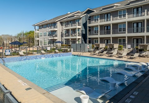 Two-Bedroom Apartments in Rowlett, TX - Village of Rowlett - Swimming Pool Features In-Water Lounge Chairs, Poolside Seating, And Sun Umbrellas.